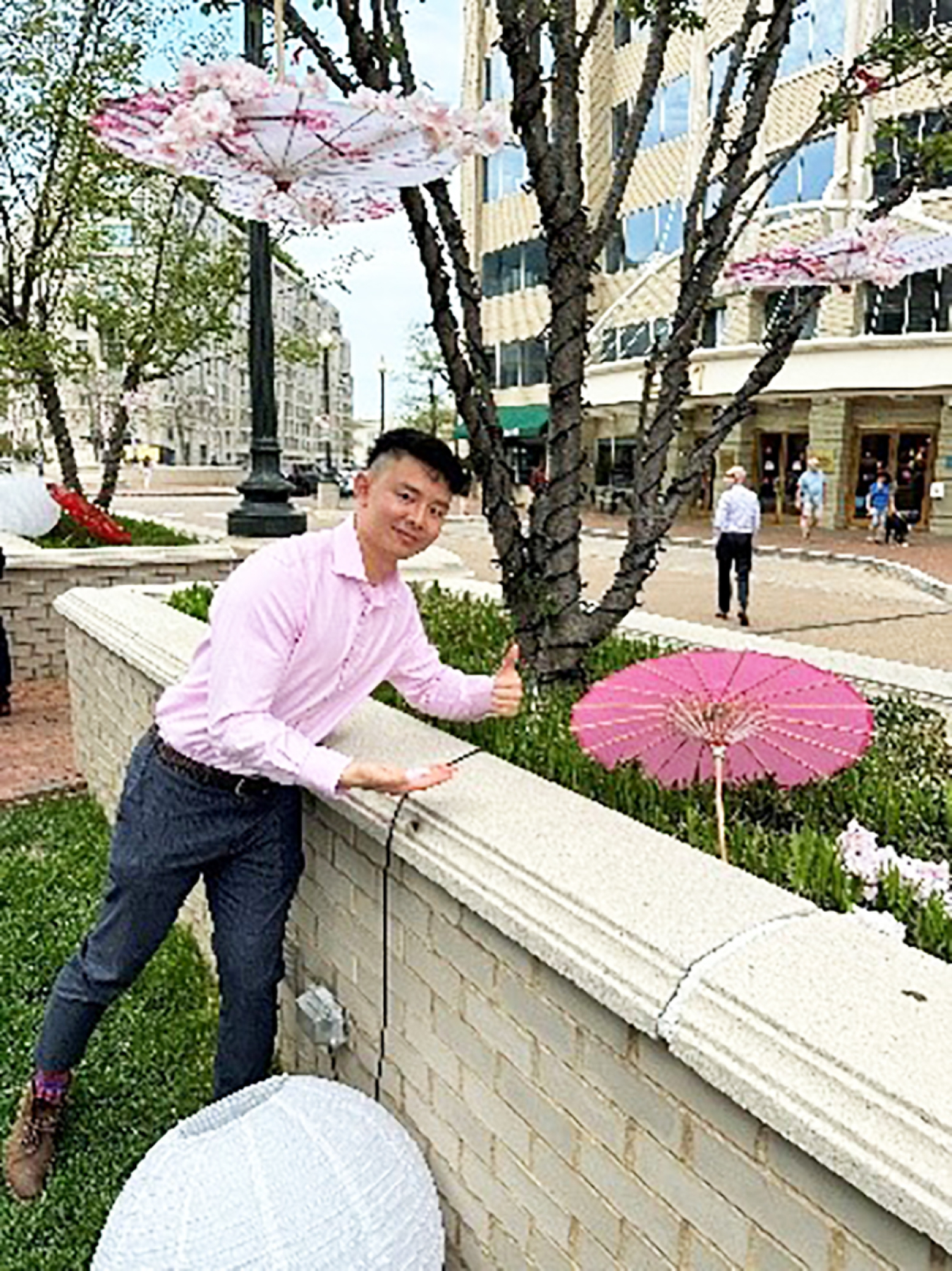 A portrait of Chris Dinh. Near him is a cherry blossom on a tree, a Japanese lantern, and a Japanese paper parasol.