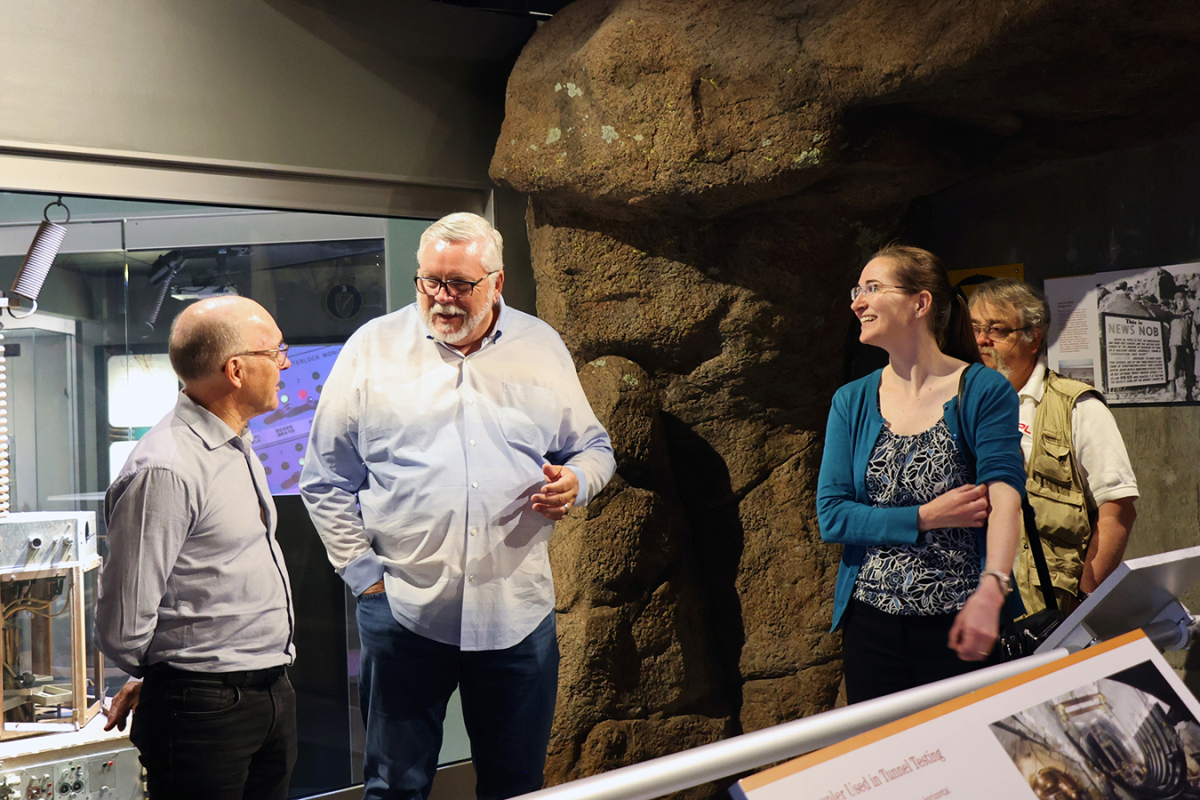 A bearded man explains something to Dr. Floyd as two woman look on in a museum environment.