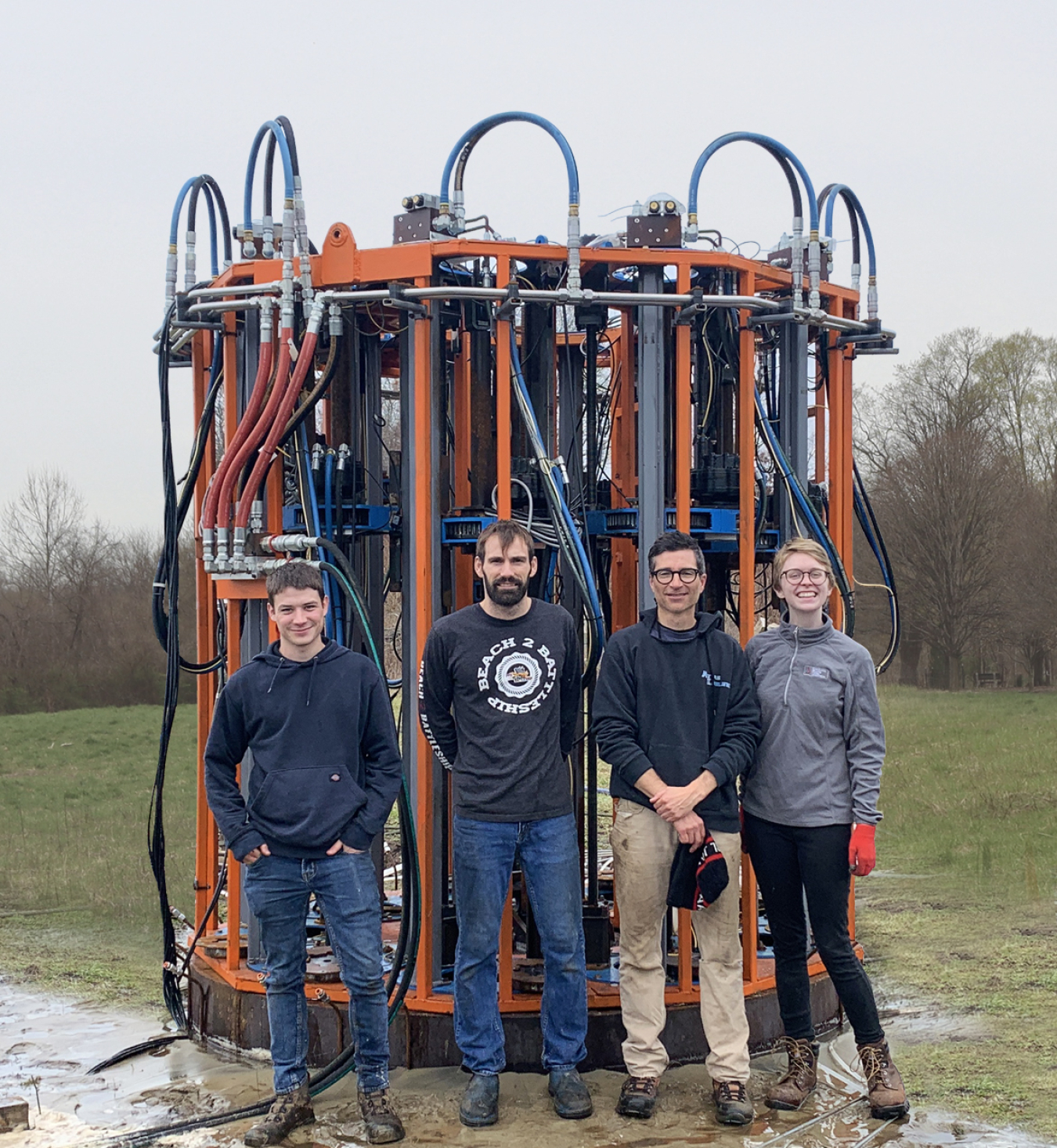 Four researchers from Triton Systems Inc, stand in front of a large anchor and its installation system. 