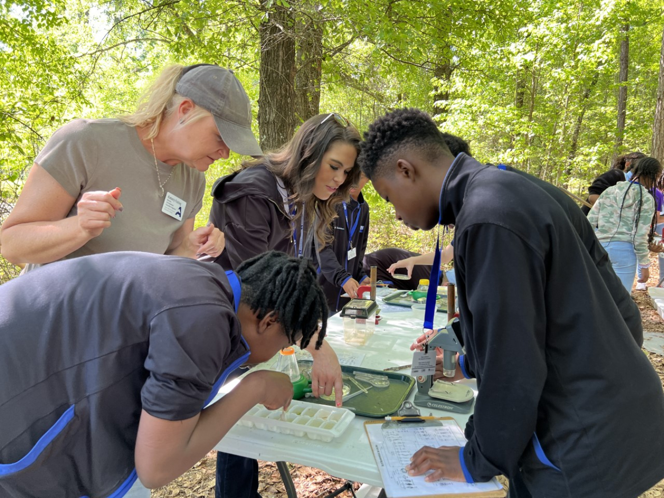 Kimberly Fickling, environmental education director at the Ruth Patrick Science Education Center, far left, and Taylor Rice, Savannah River Nuclear Solutions education outreach specialist, at right of Fickling, assist students in identifying macroinvertebrates under a microscope.