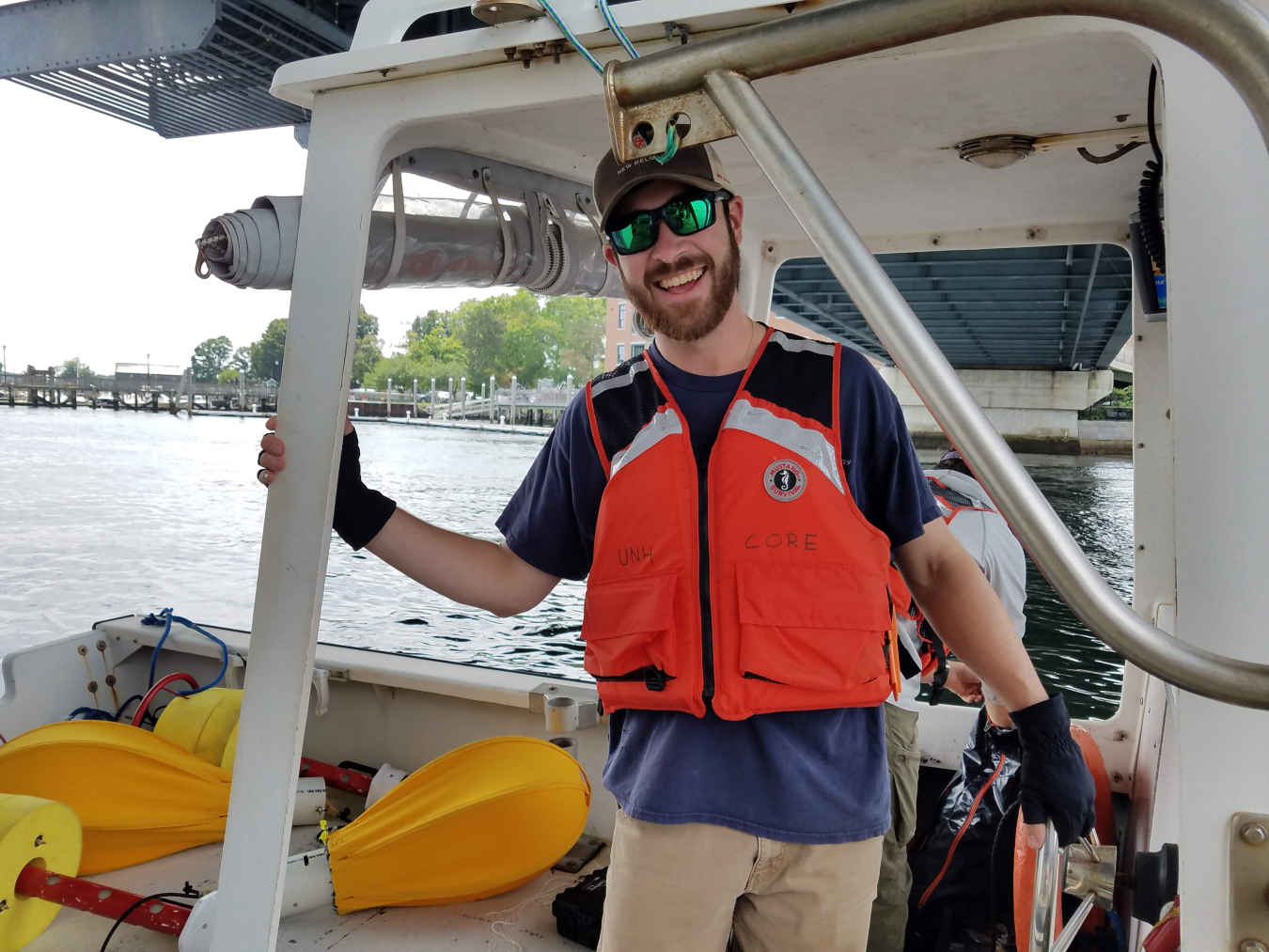 Patrick O'Byrne smiles as he stands at the wheel of a small boat under a bridge in the middle of a river