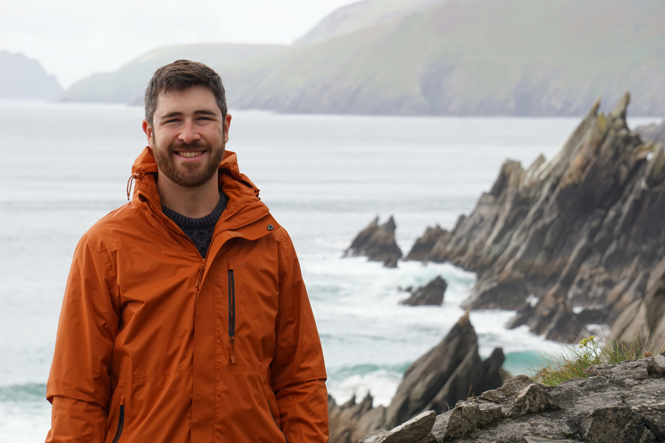 Patrick O’Byrne standing on a rocky coastline with the ocean behind him