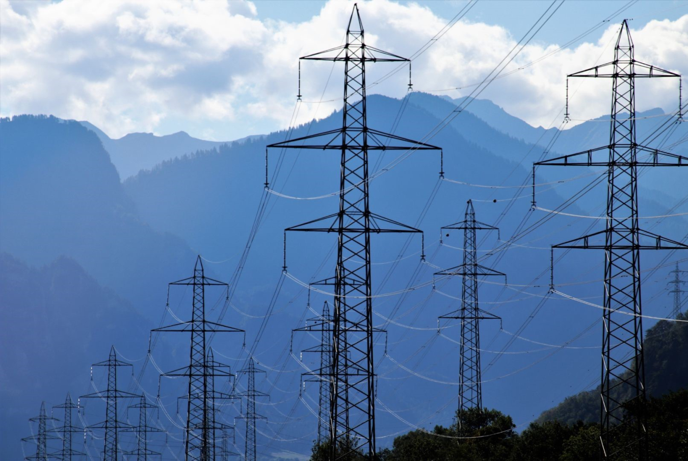 Transmission towers and power lines against a deep blue sky with mountains in the background