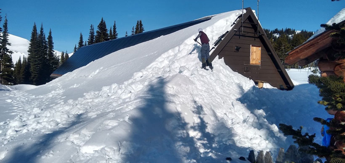 Photo of a man shoveling snow off of the powerhouse building roof.