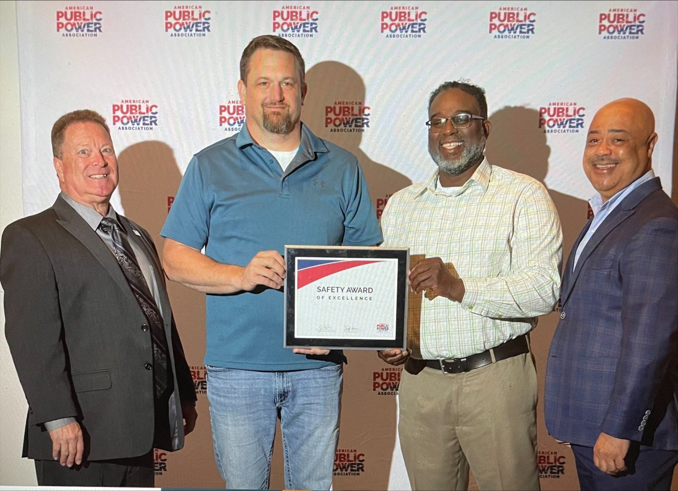 Four males in front of a background. Middle two are holding a certificate