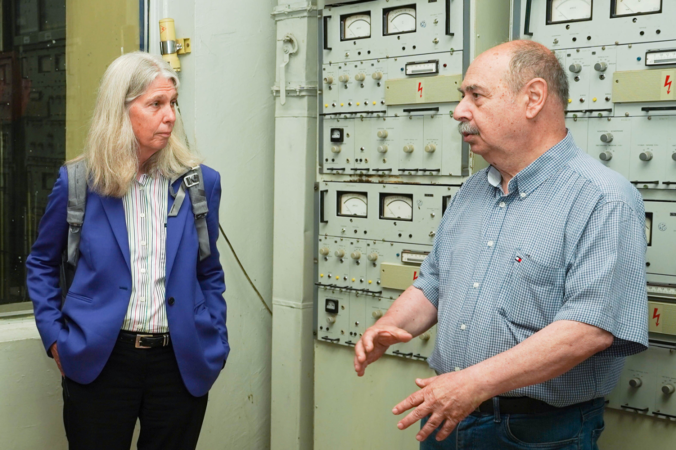 Administrator Hruby listens to a man while they stand in a room with switches and gauges on the wall.