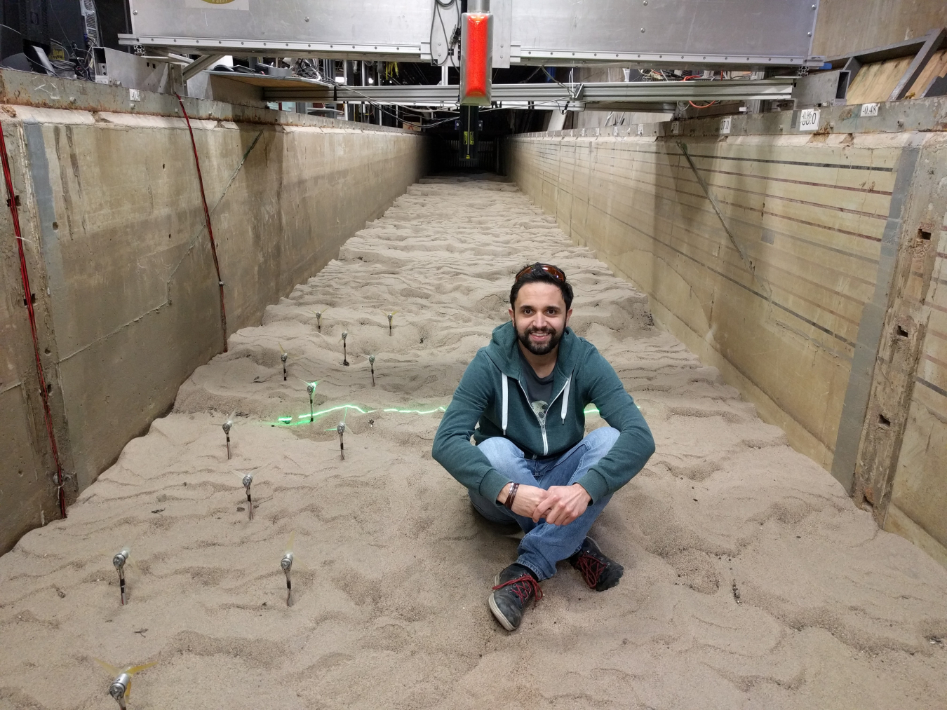 Mirko Musa sitting on sand inside a concrete channel, which contains a few miniature turbines embedded in the sand