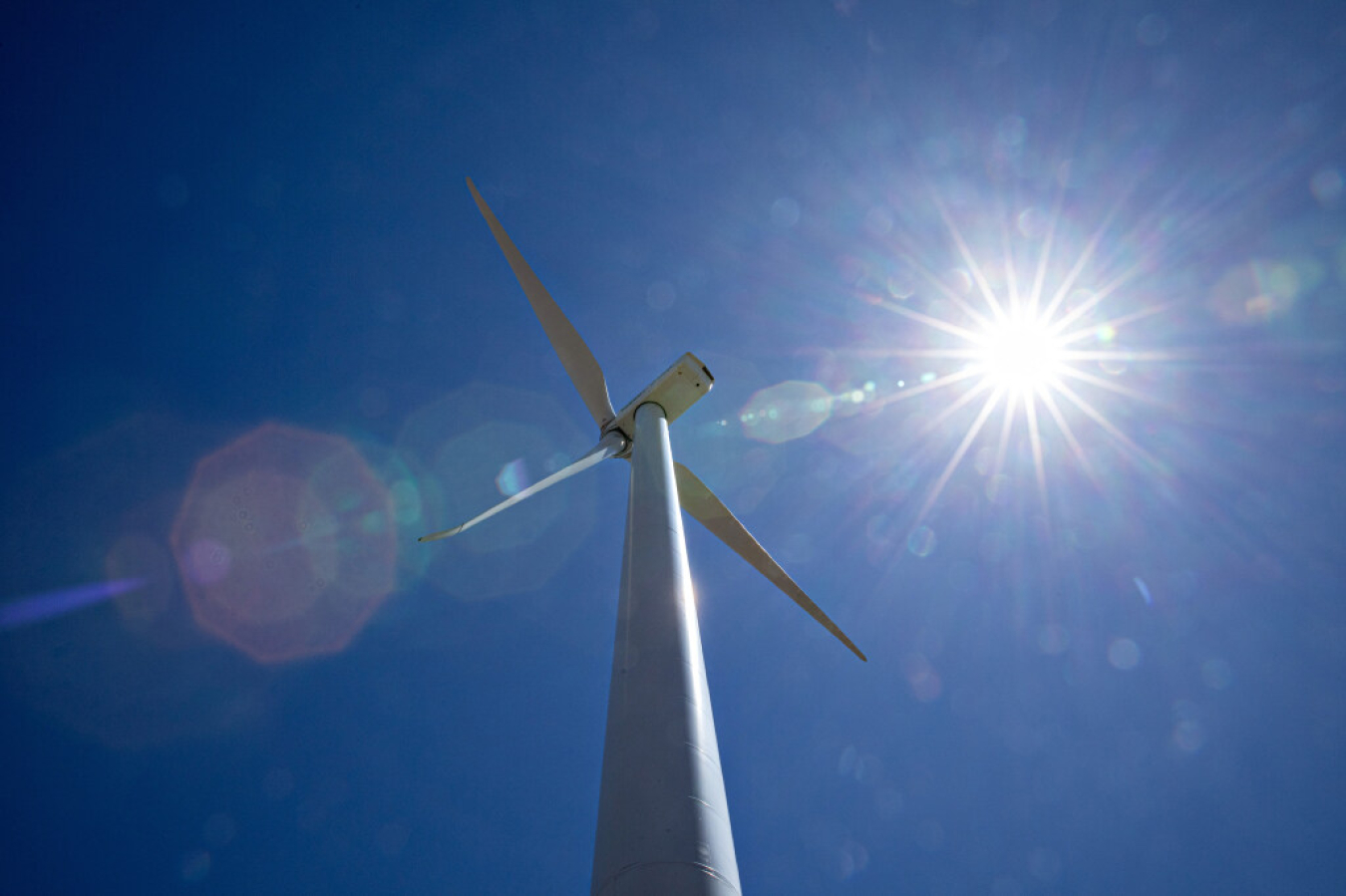 The sun shines down on a wind turbine. 