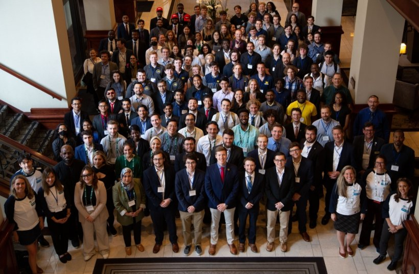 A large group of people standing in a foyer looking up at a photographer on a second story 