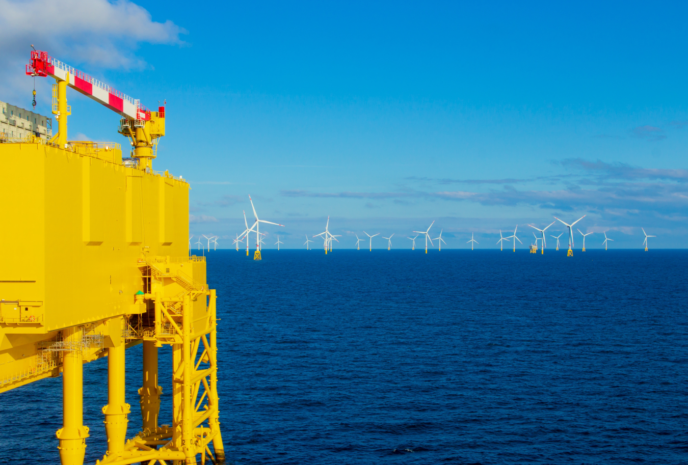 An ocean-bound HVDC substation in front of several ocean-bound wind turbines.