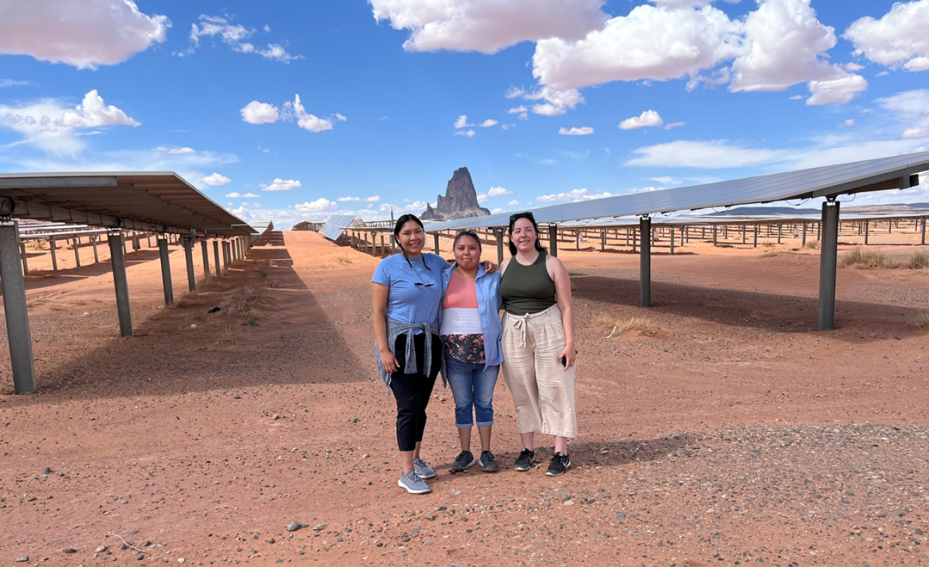 Three Native American woman in front of a large solar installation in the desert.