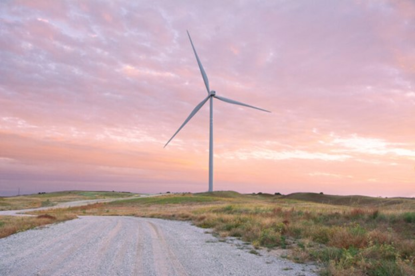 The sun sets on a wind turbine in a grassy area.