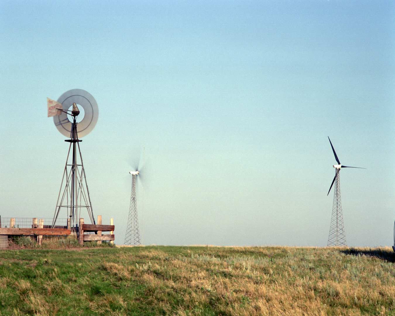 Two modern wind turbines stand near an old-fashioned windmill on a grassy plain.