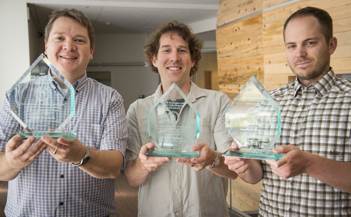 HydroGEN experts Todd Deutsch, James Young, and Myles Steiner hold glass awards while smiling.