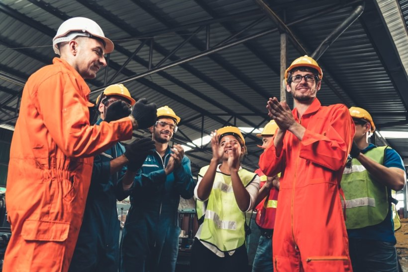 a group of people applauding. They are wearing hardhats and coveralls. 