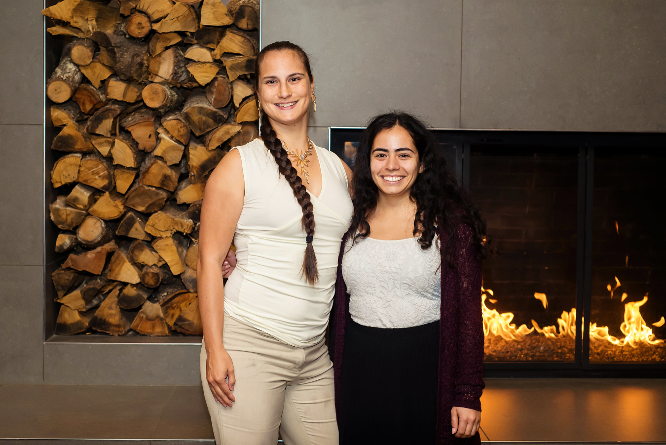 Two people pose and smile for the camera in front of an indoor fireplace.