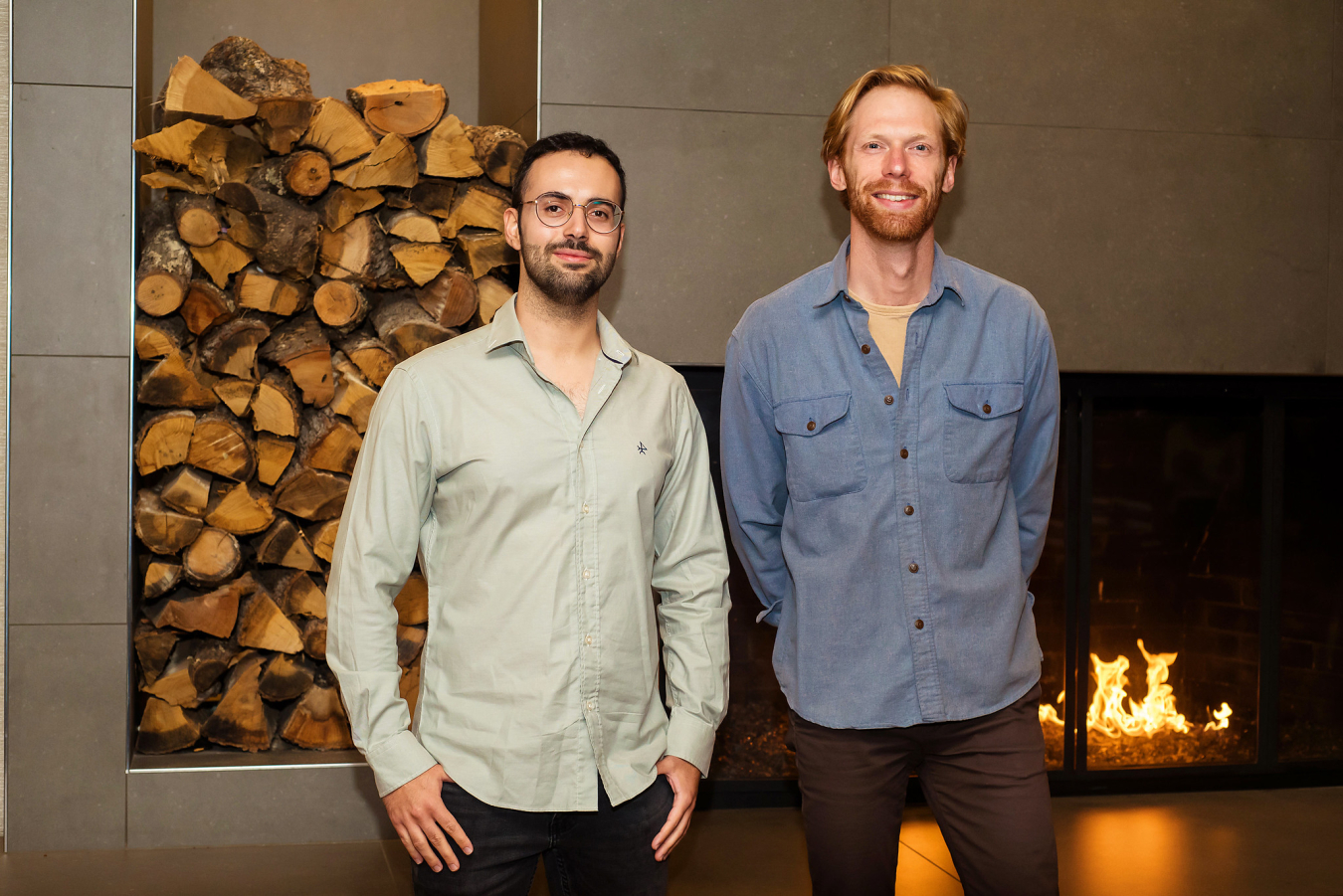 Two people pose and smile for the camera in front of an indoor fireplace.