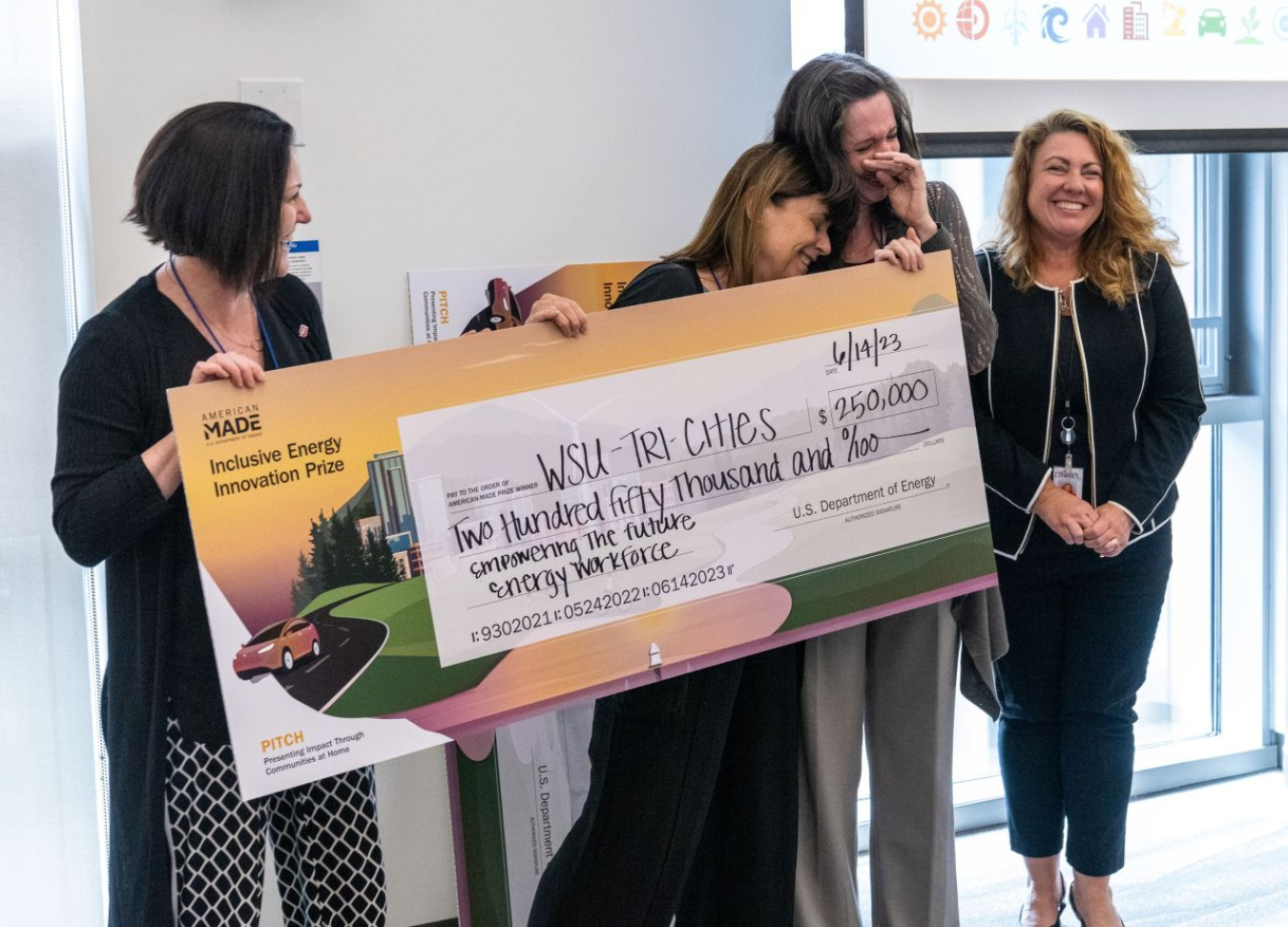 Four people smile and wipe away tears of joy while holding a large check for $2500,000.