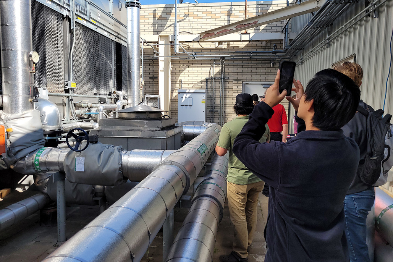 A group of people taking pictures of an HVAC system on top of a building.