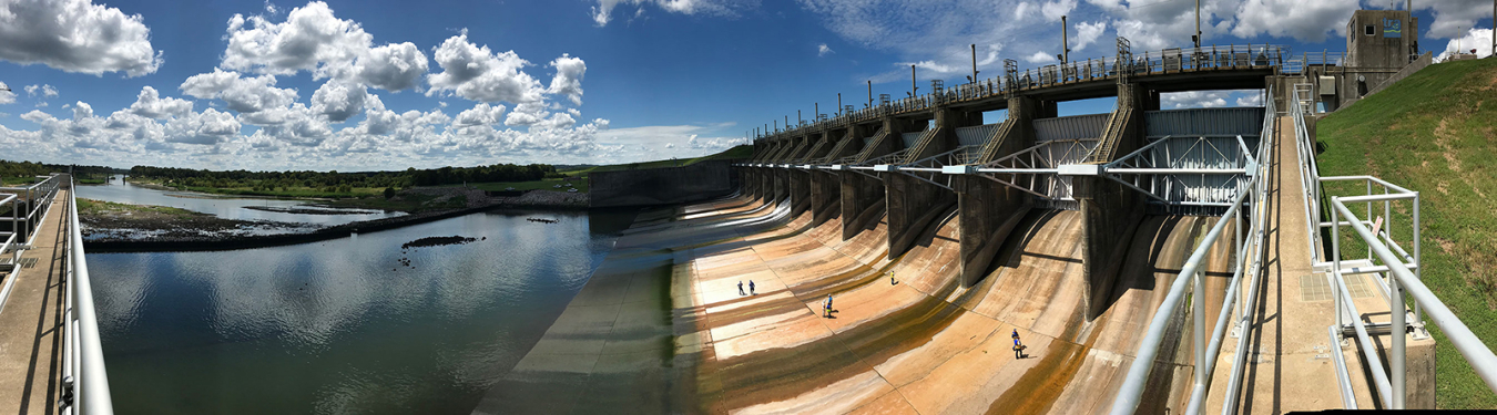 Hydropower workers walk along the spillway of an East Texas Electric Cooperative dam under a blue sky with fluffy clouds.