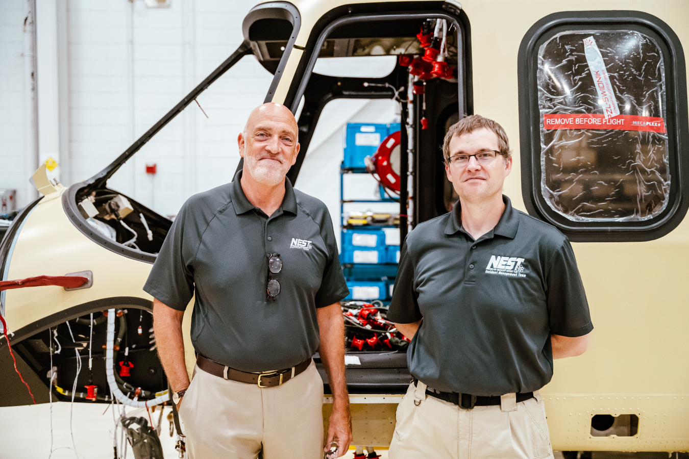 Two men stand in front of an unfinished helicopter chassis.