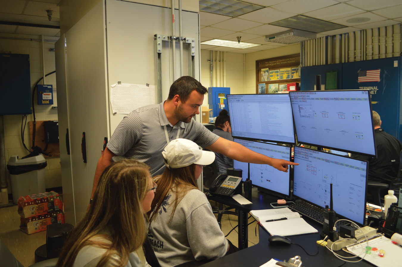 UCOR chemical operator apprentices sit in front of computer screens with man pointing at screen.