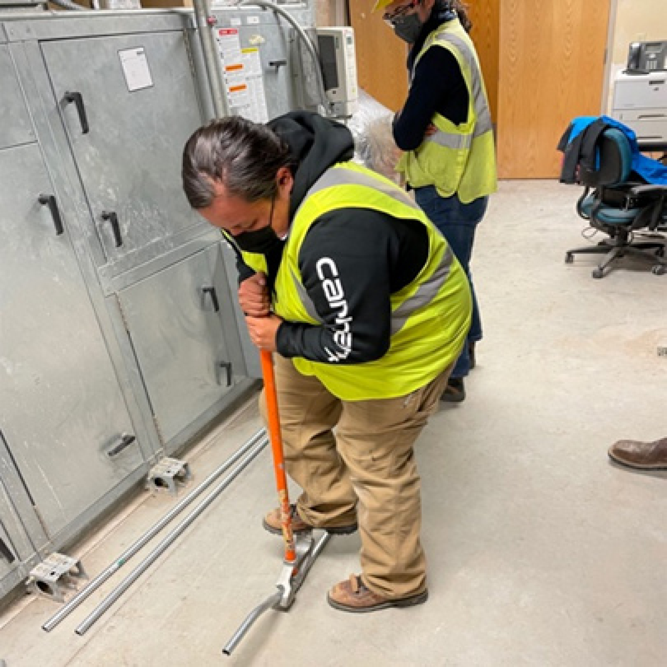 A man in construction vest uses his foot to adjust electrical equipment.