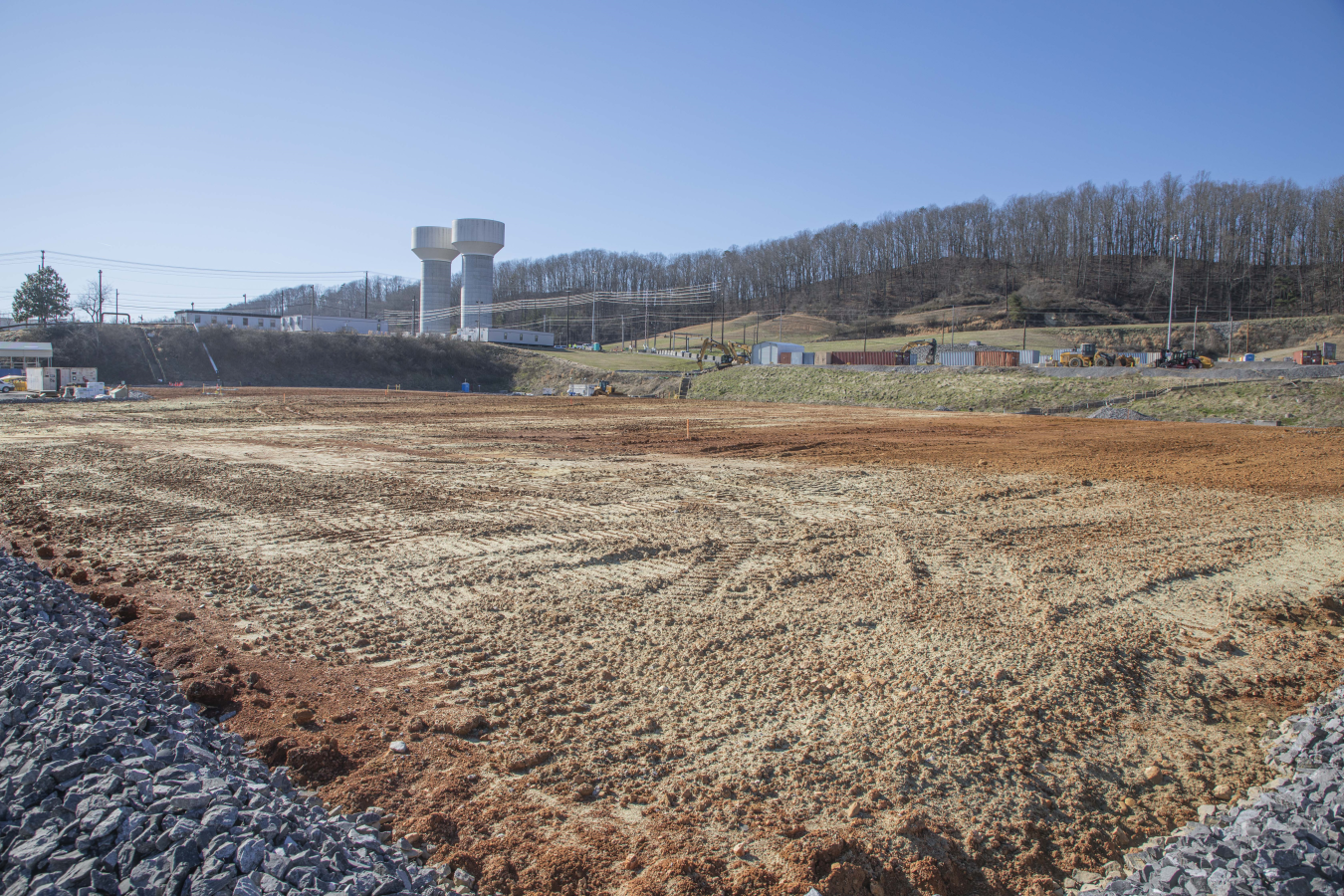 A large dirt filed with trees and two tower buildings in the background