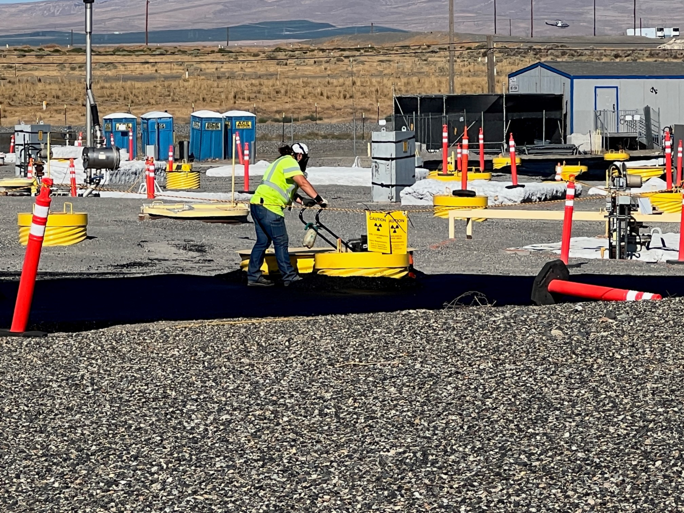 Crews operate compactors to level and compress surface barrier asphalt in tight areas around infrastructure at the U Tank Farm on the Hanford Site.