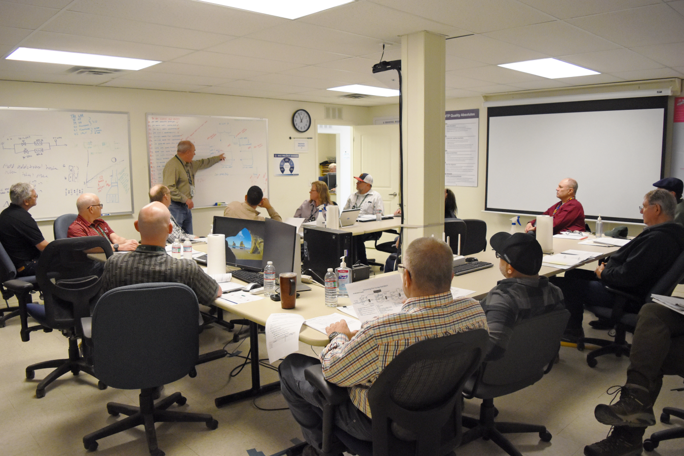 A group of employees sit in a lecture room listening to a man giving a presentation