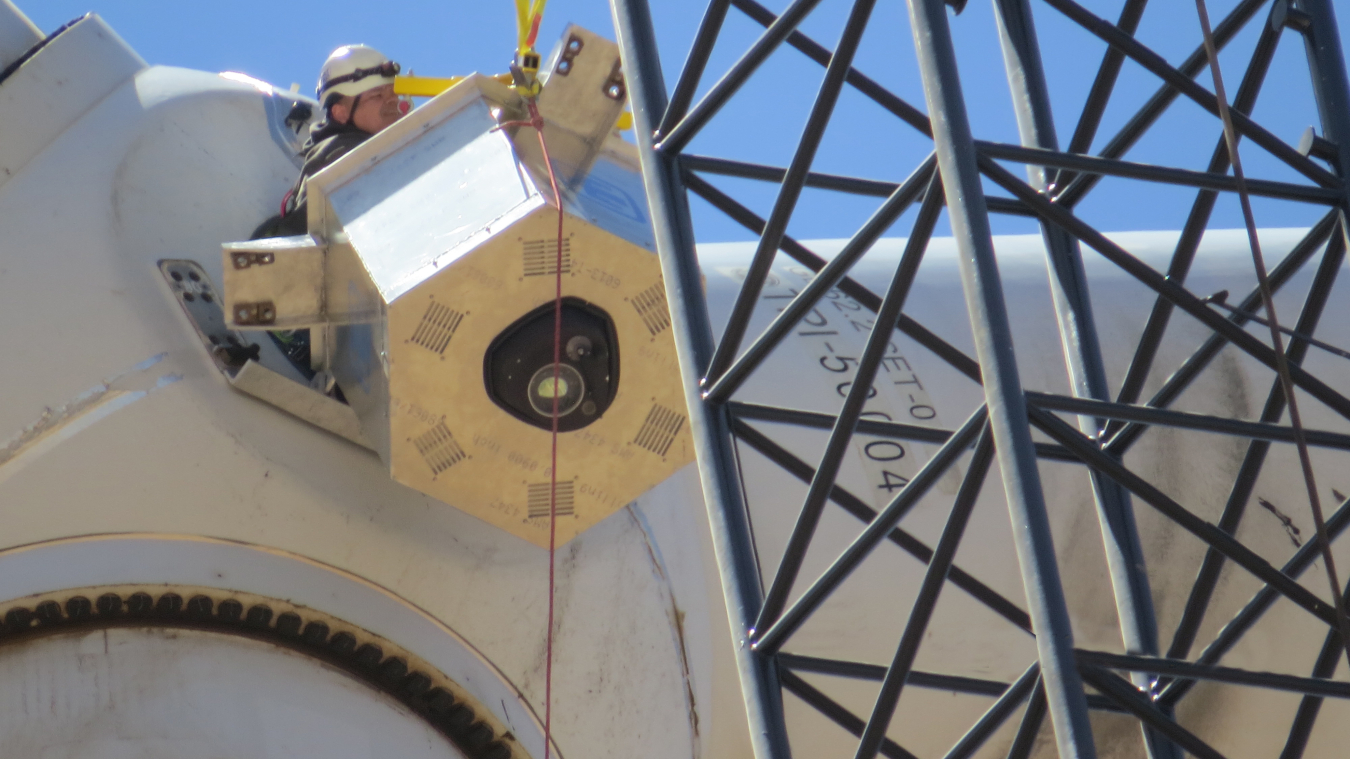 A man installs a spinning laser onto a wind turbine. 