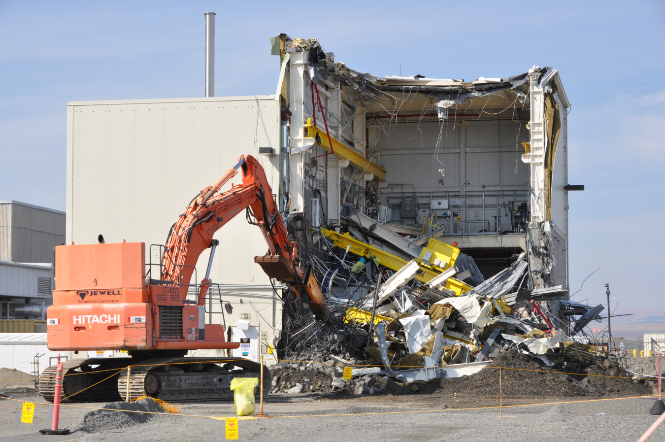 Machines with long arm performing demolition on old building.