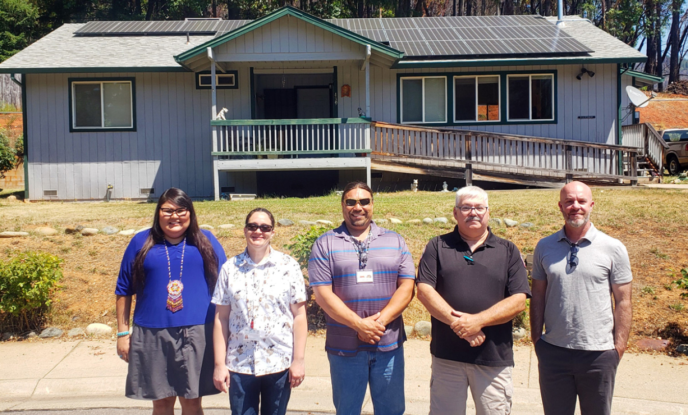 5 people pose in front of a house with rooftop solar panels.