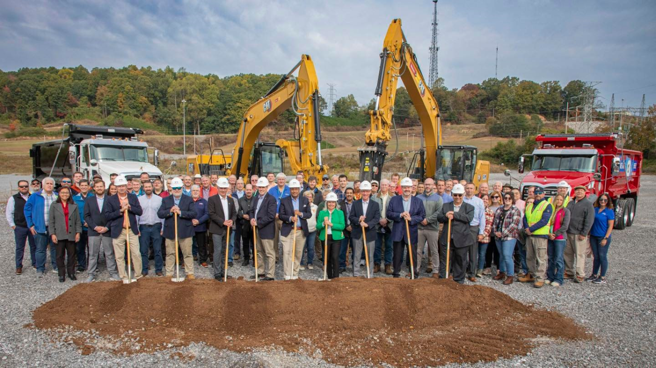 Large group of people pose for a picture, some holding shovels and wearing hard hats