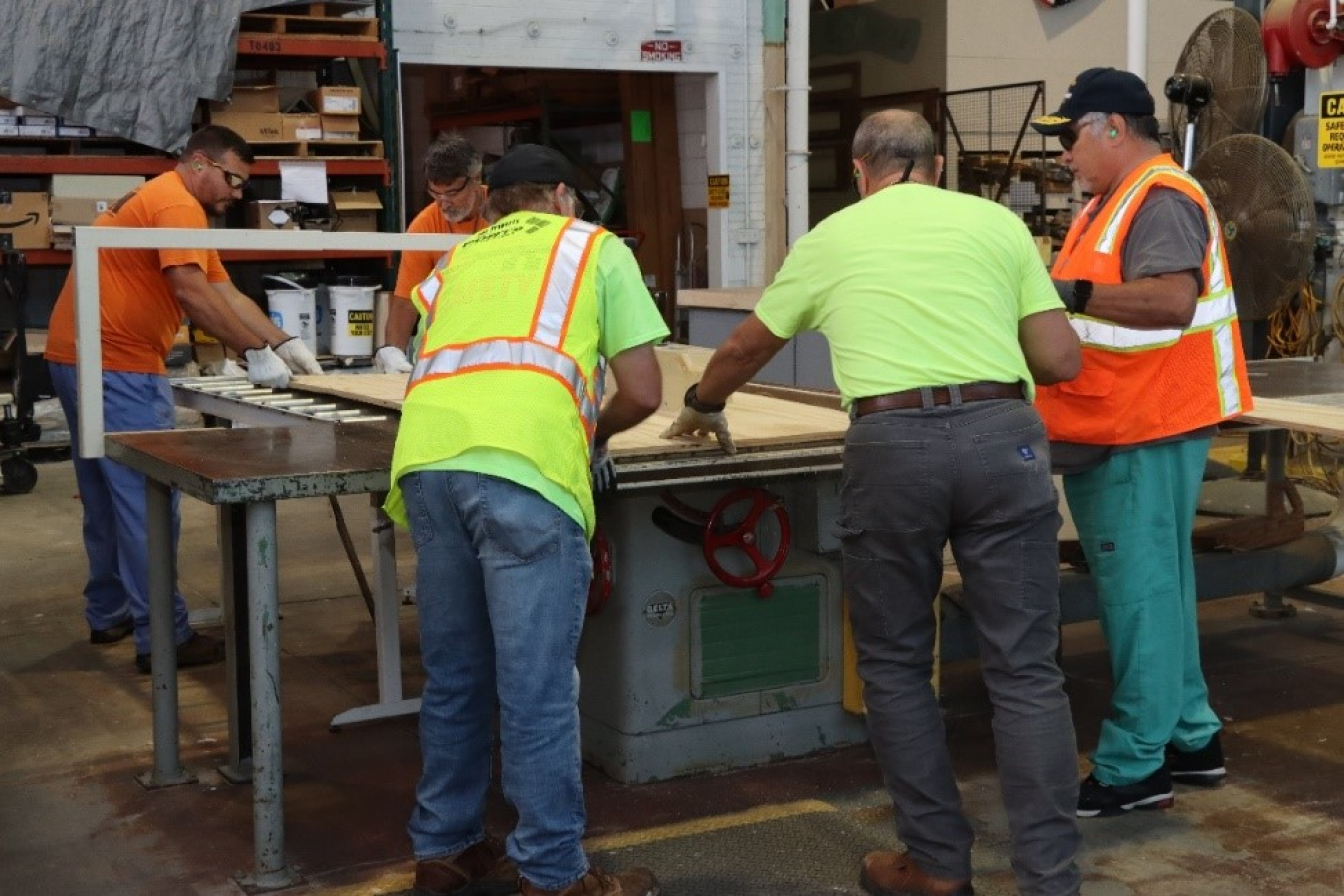 Group of men working around the same workshop table inside building. 