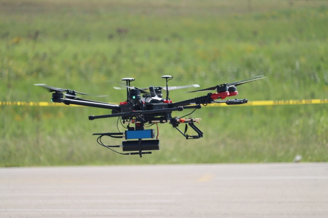 A black and red drone flying over grass