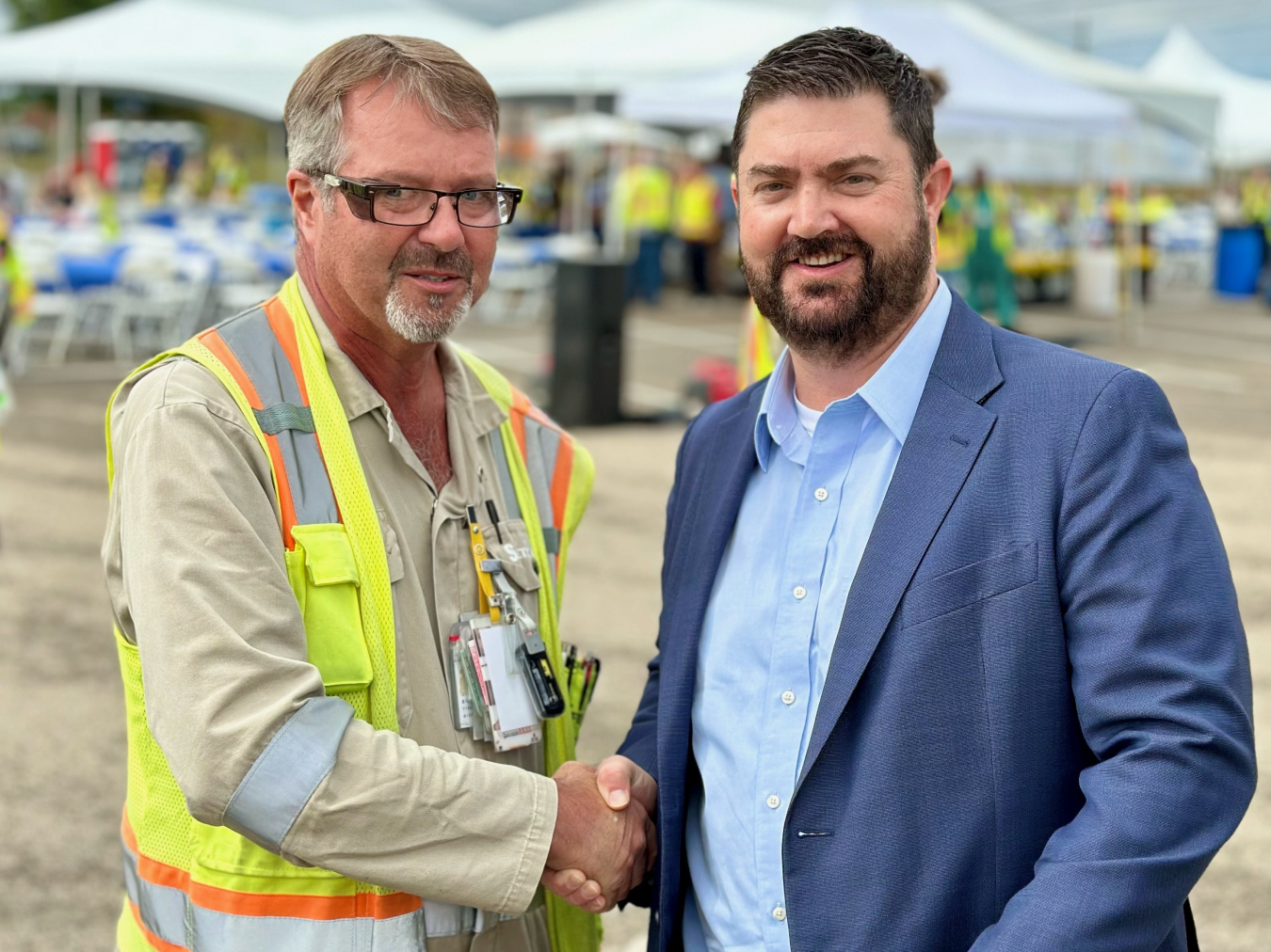 Two men shake hands and smile for a photo.