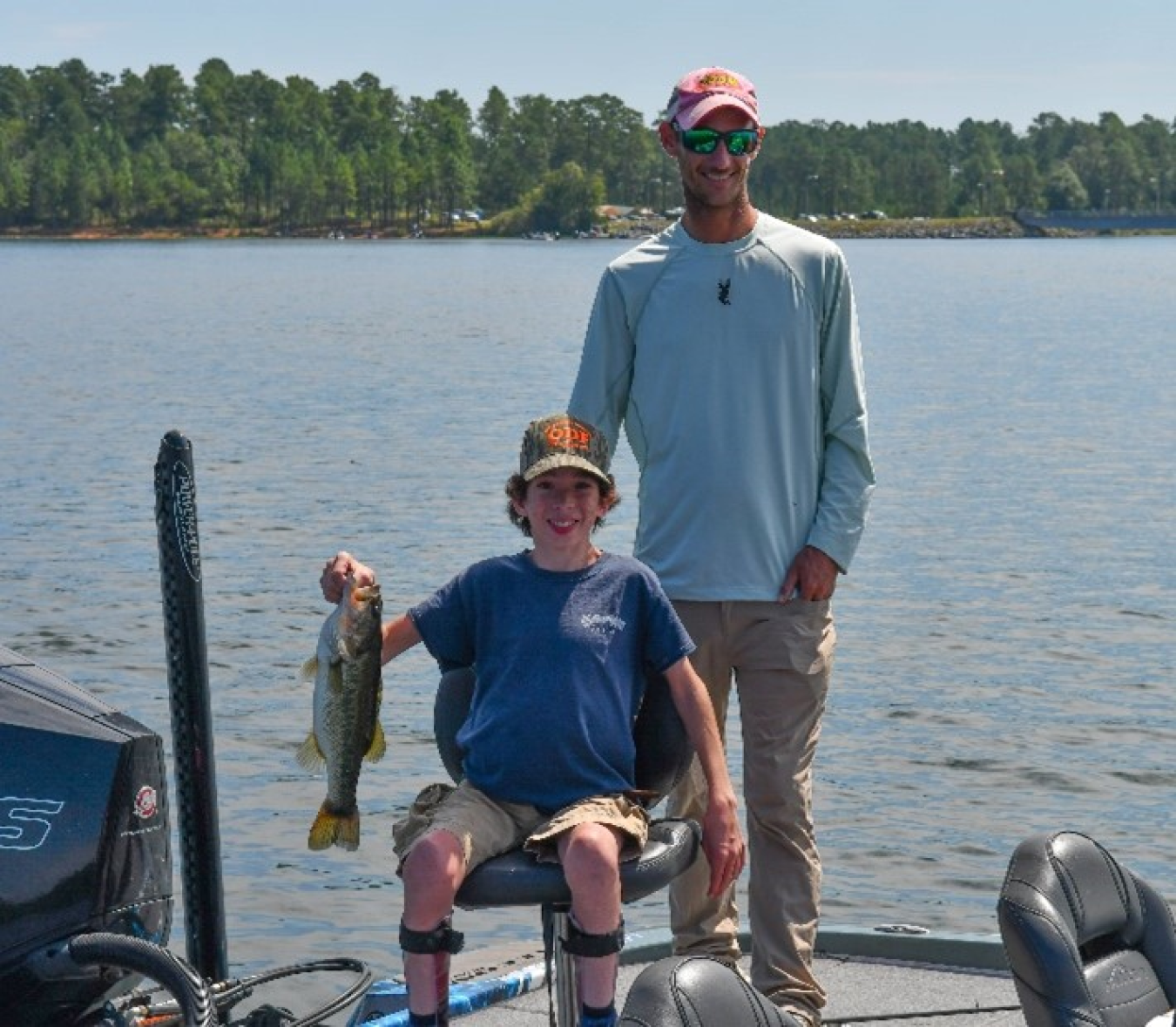 Man and boy on a boat in a lake, the boy is holding up a fish