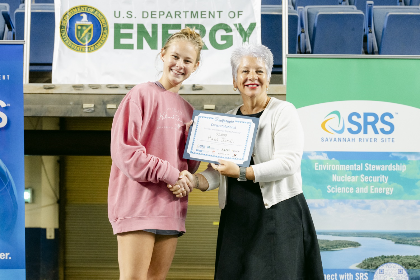 A high school senior shakes hands with a woman awarding her a scholarship certificate