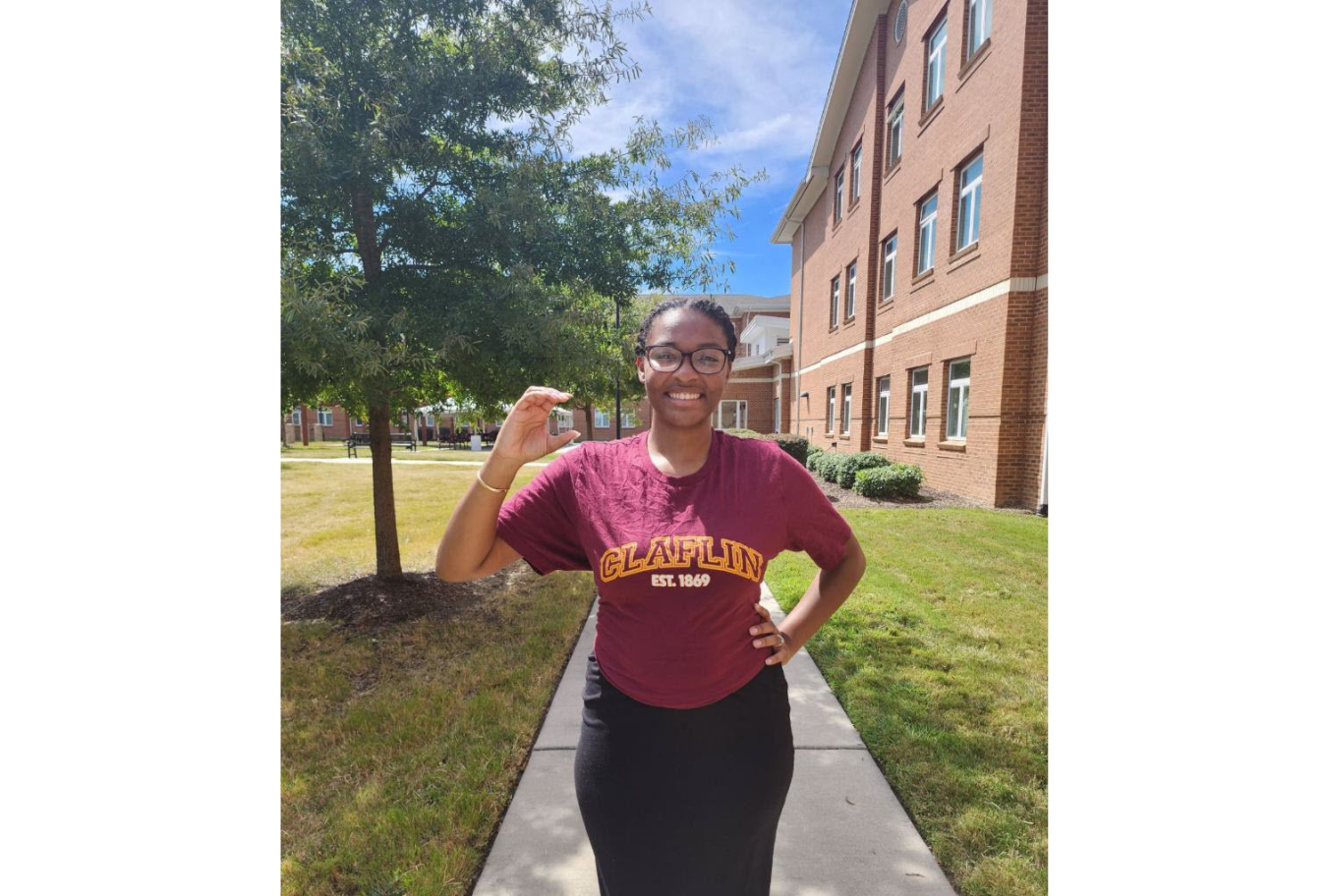 Shelby Thomas posing outside with a building in the background. She is wearing a t-shirt that says "Claflin Est. 1869" and posing with her hand in a "C" shape.