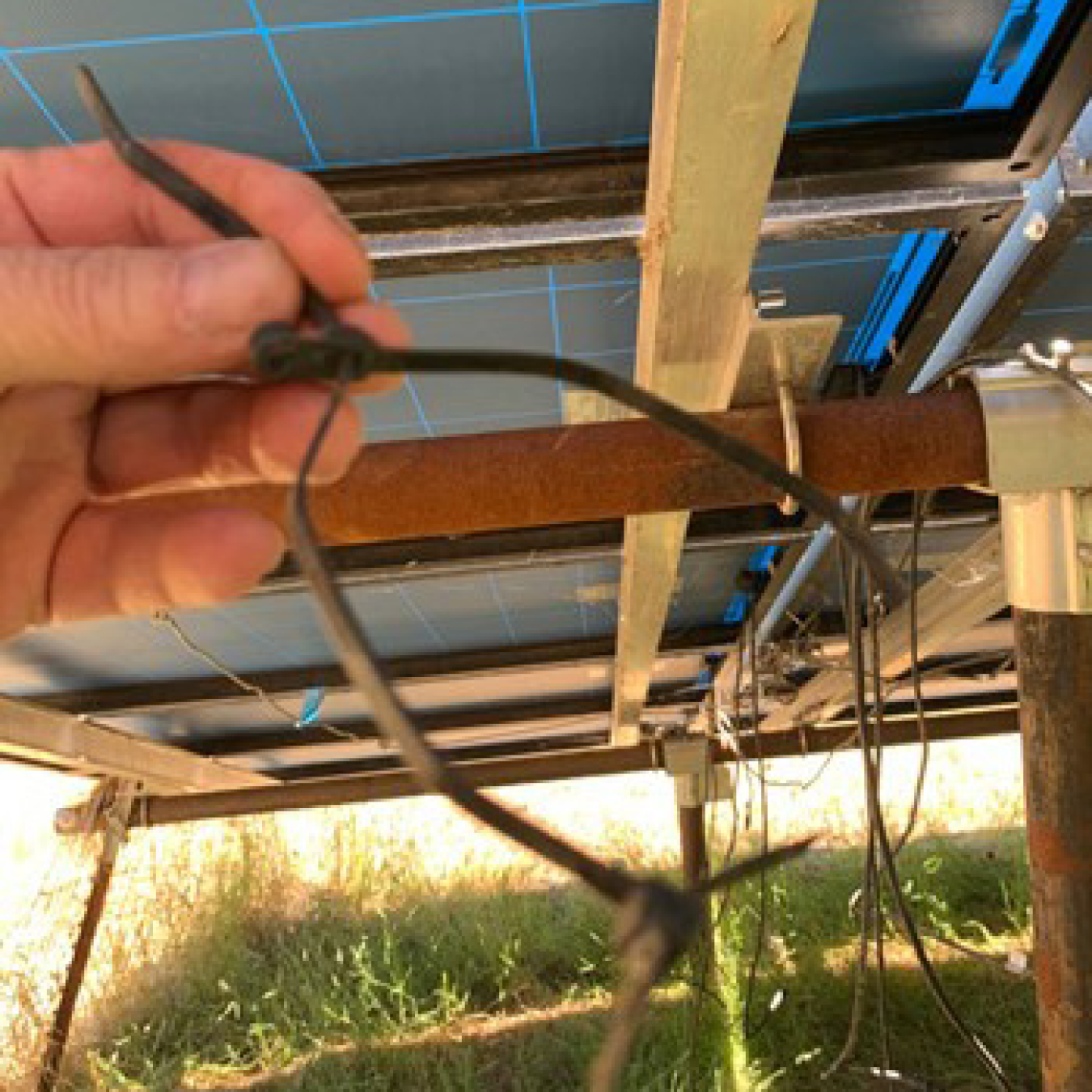 Someone's hand holding a broken cable tie underneath a frame holding solar photovoltaic panels.