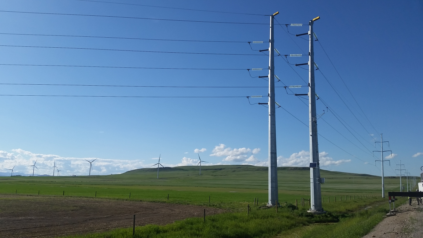 Transmission line towers in the foreground with hills in the background on a sunny day. 