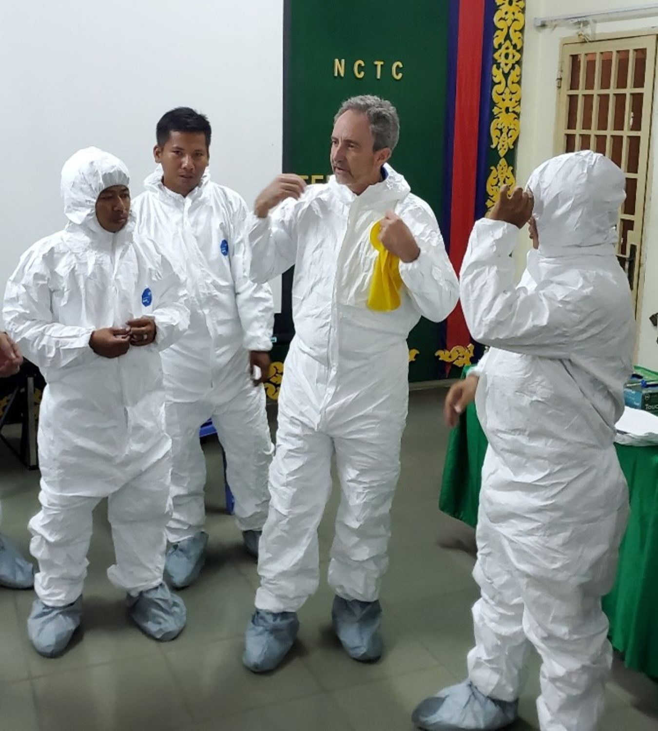 Four men in protective clothing discuss emergency response.