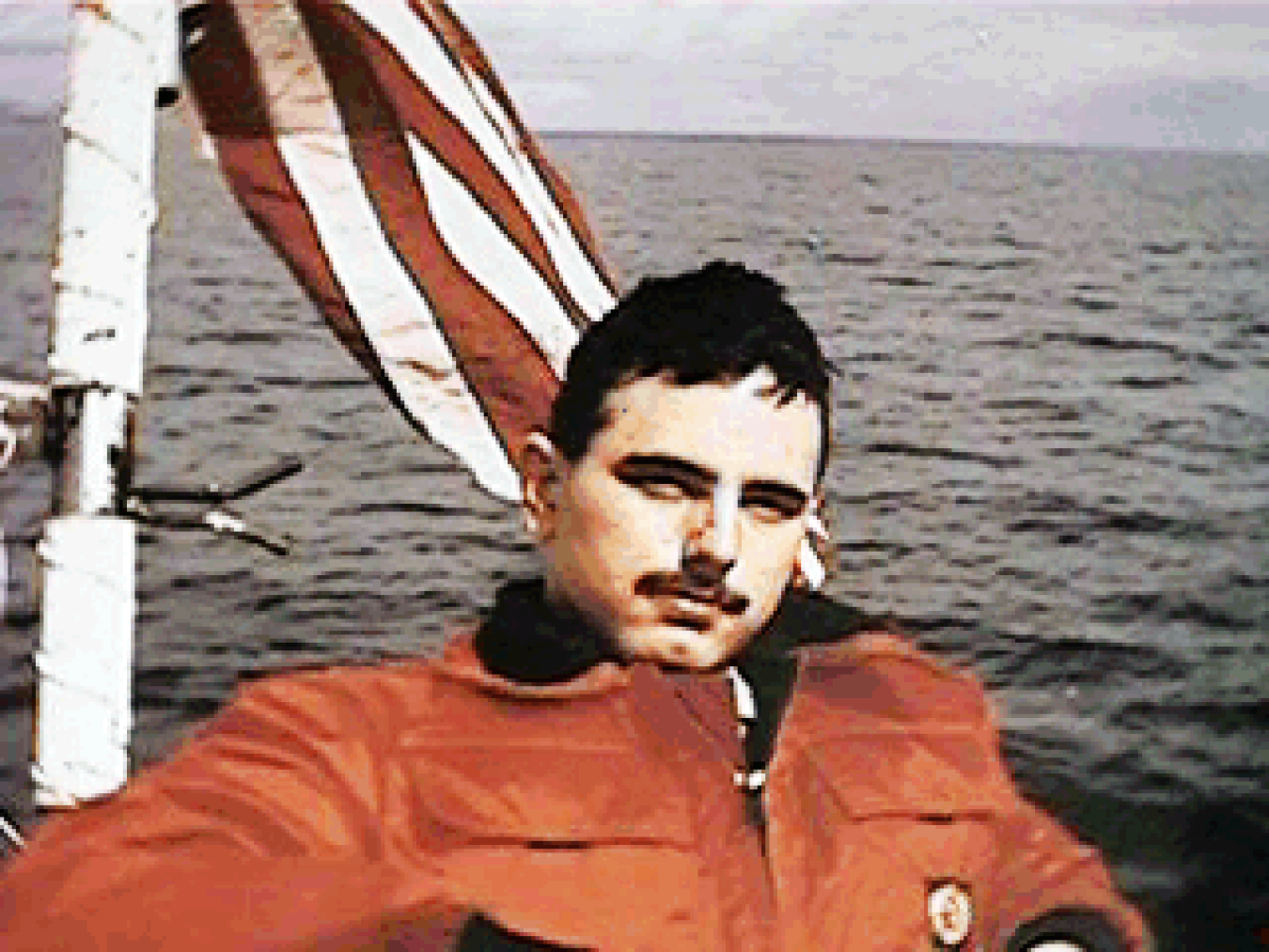 Man in a jacket on a boat that is flying the American flag behind him