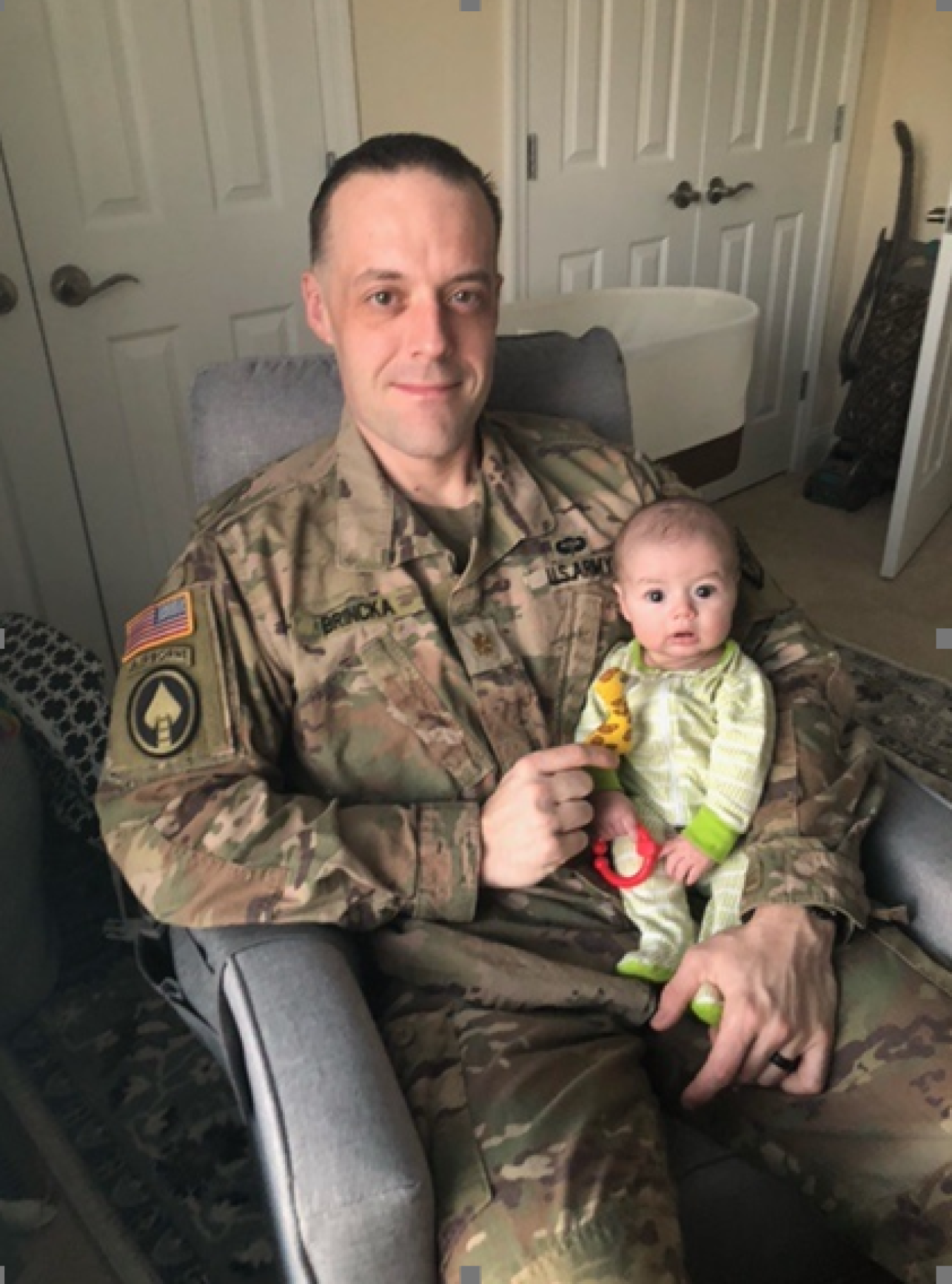 A portrait of Bradley Brincka dressed in uniform with a baby in his lap.