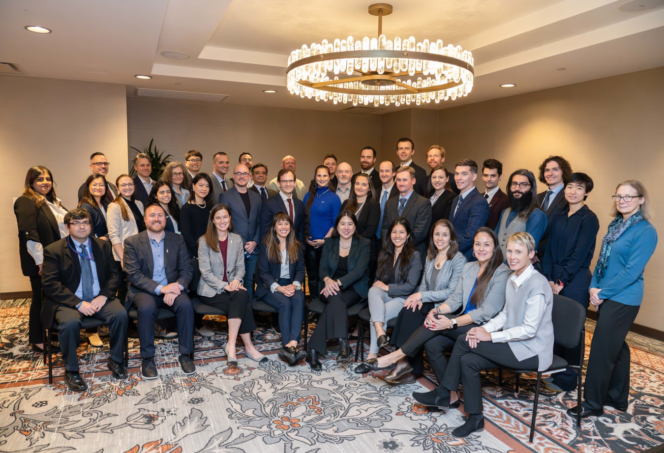 A group of 40 people professionally dressed, pose in a hotel meeting room and smile for a photo.