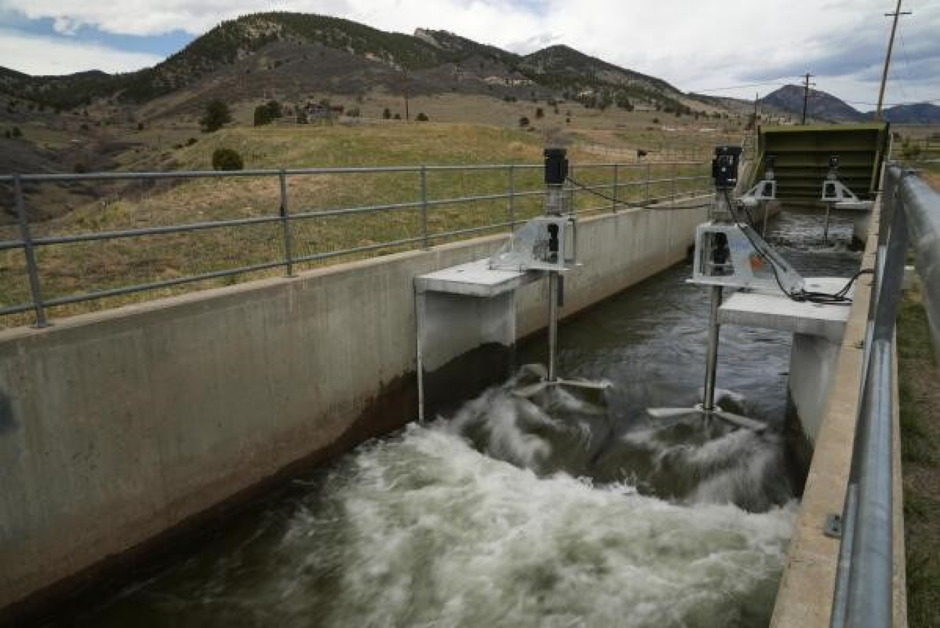 Two turbines situated in a narrow waterway in front of mountains.