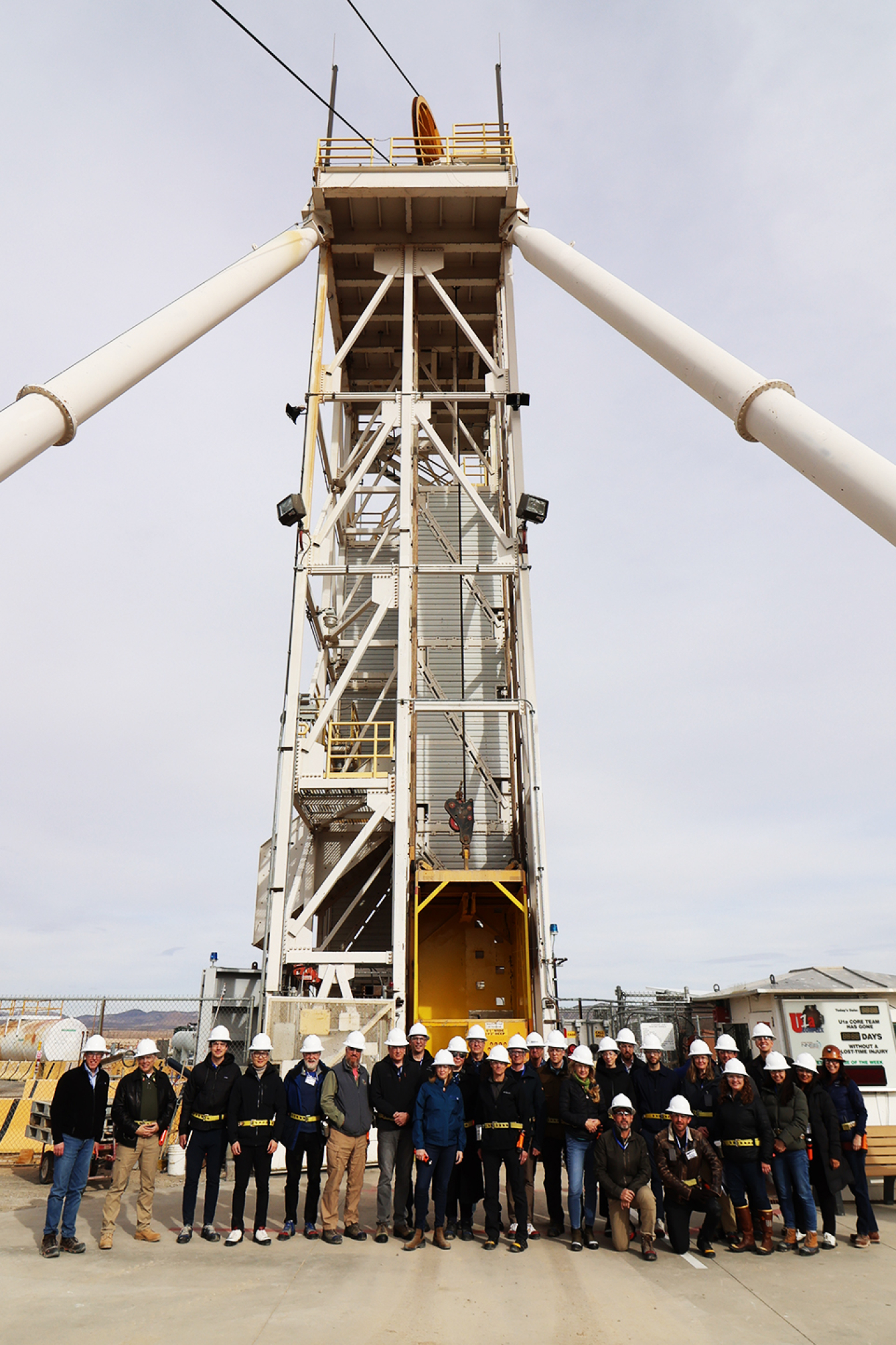 A large group of people poses outside in front of a large, metal tower