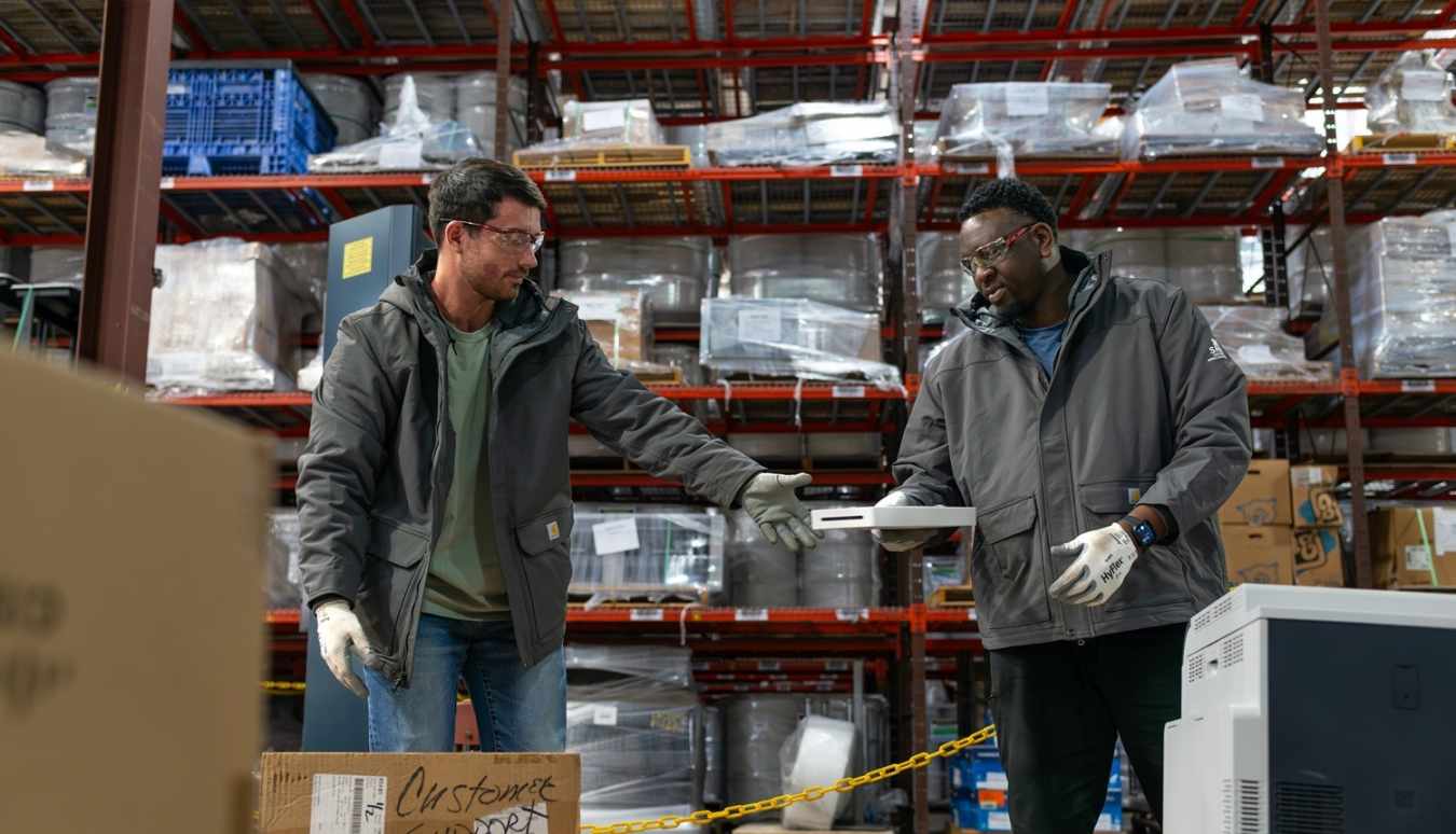 Two workers pass materials in a white box to each other 