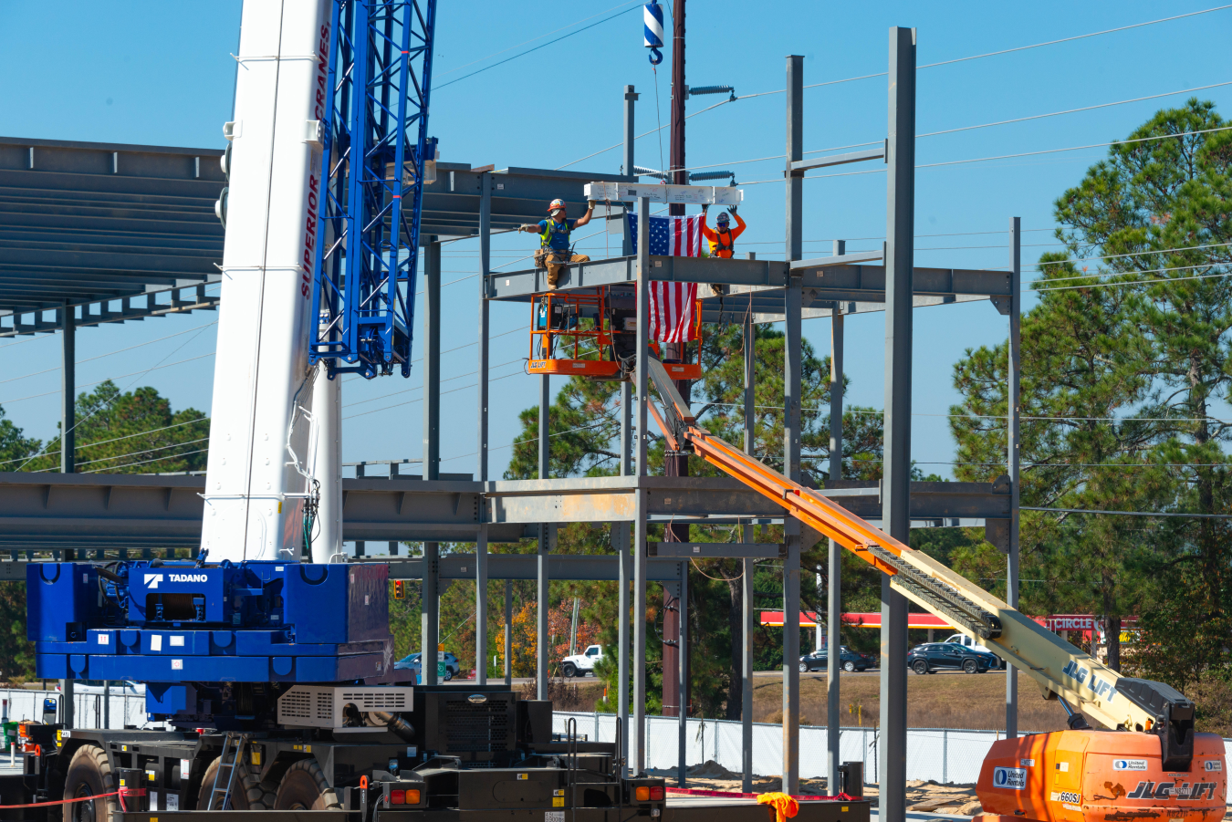 Crews on a crane with a US flag elevated to place the last steel  piece to the steel structure.